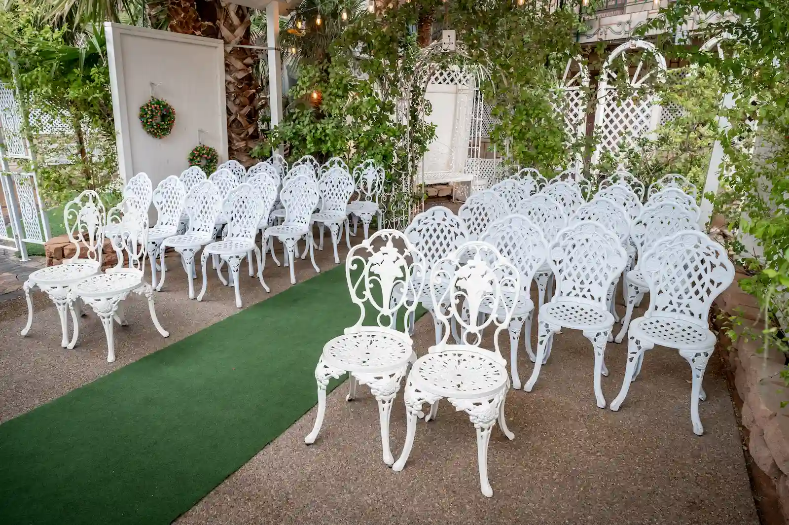 Bell Garden outdoor wedding venue with ornate white iron chairs, green aisle runner, and garden arbor at Viva Las Vegas