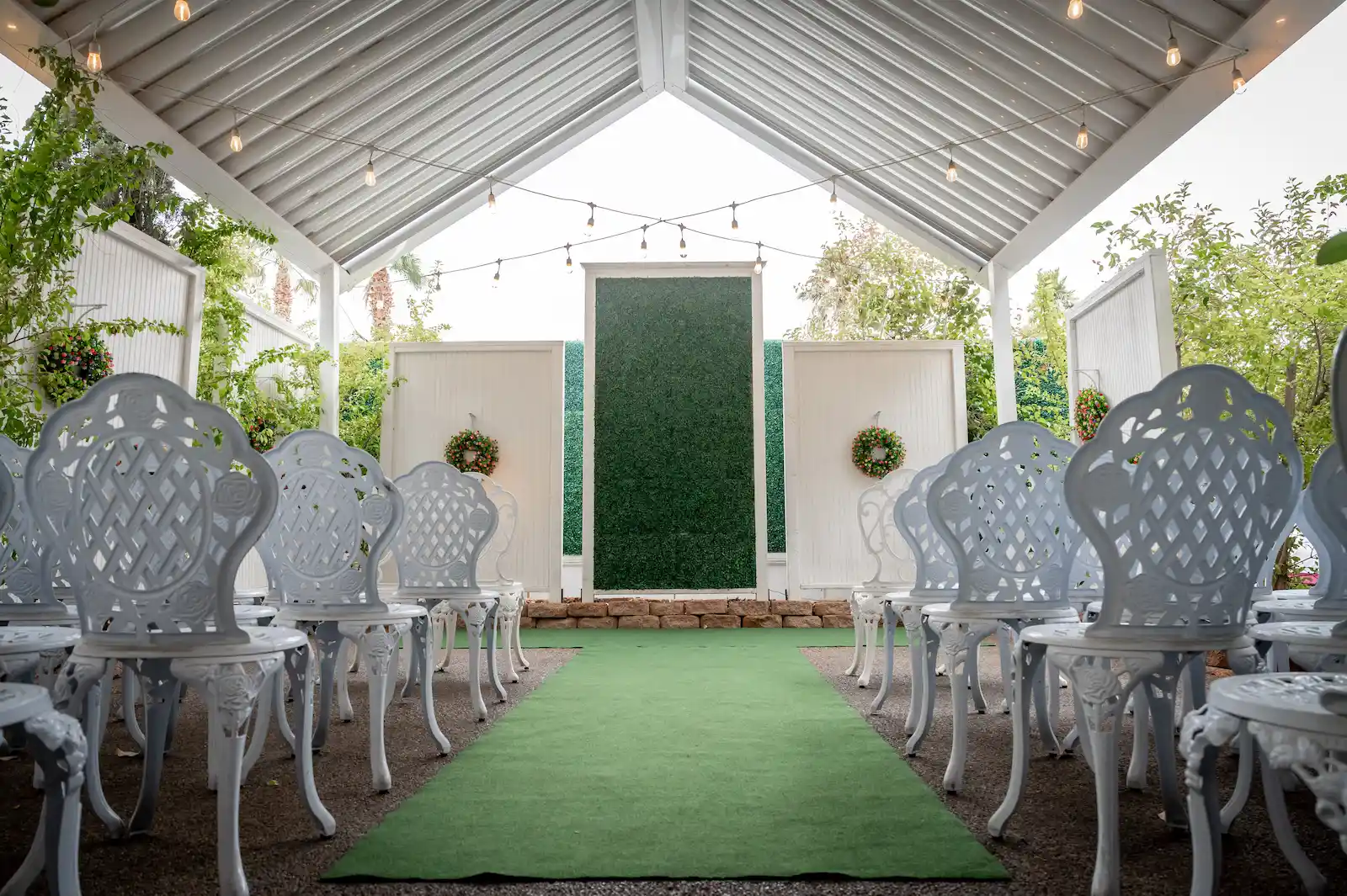 Bell Garden outdoor wedding ceremony setup with green hedge backdrop, white iron chairs, and string lights at Viva Las Vegas