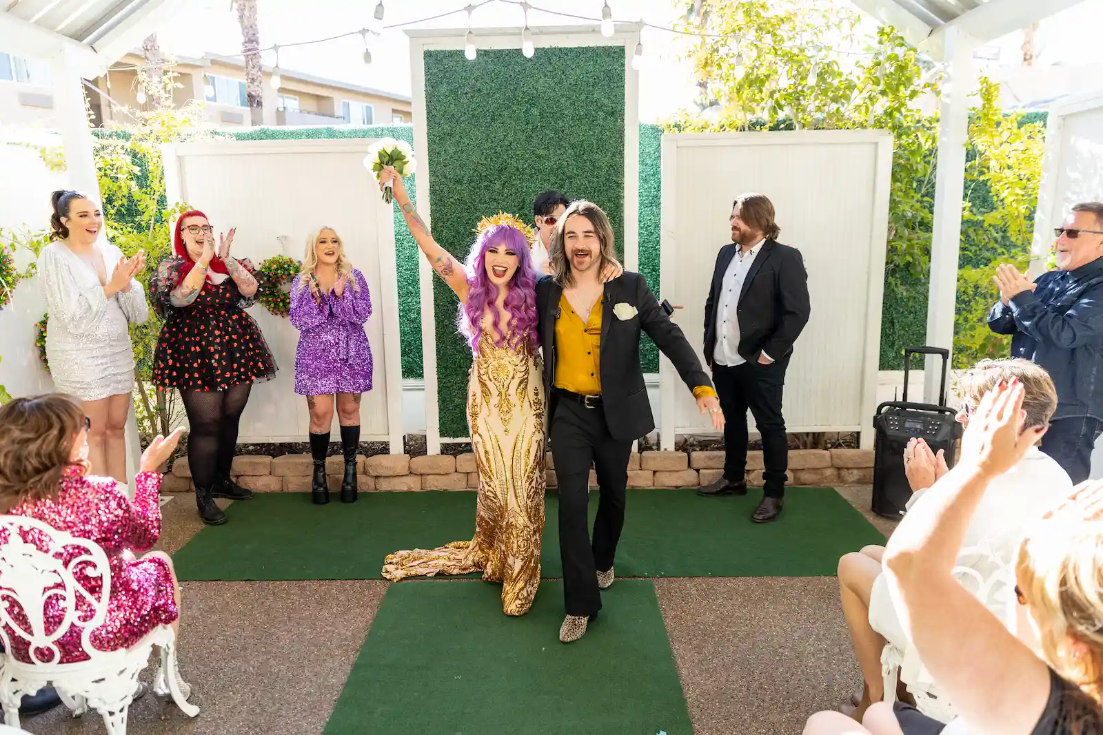 Bride in gold sequin dress with purple hair celebrating recessional with guests at outdoor Las Vegas garden wedding