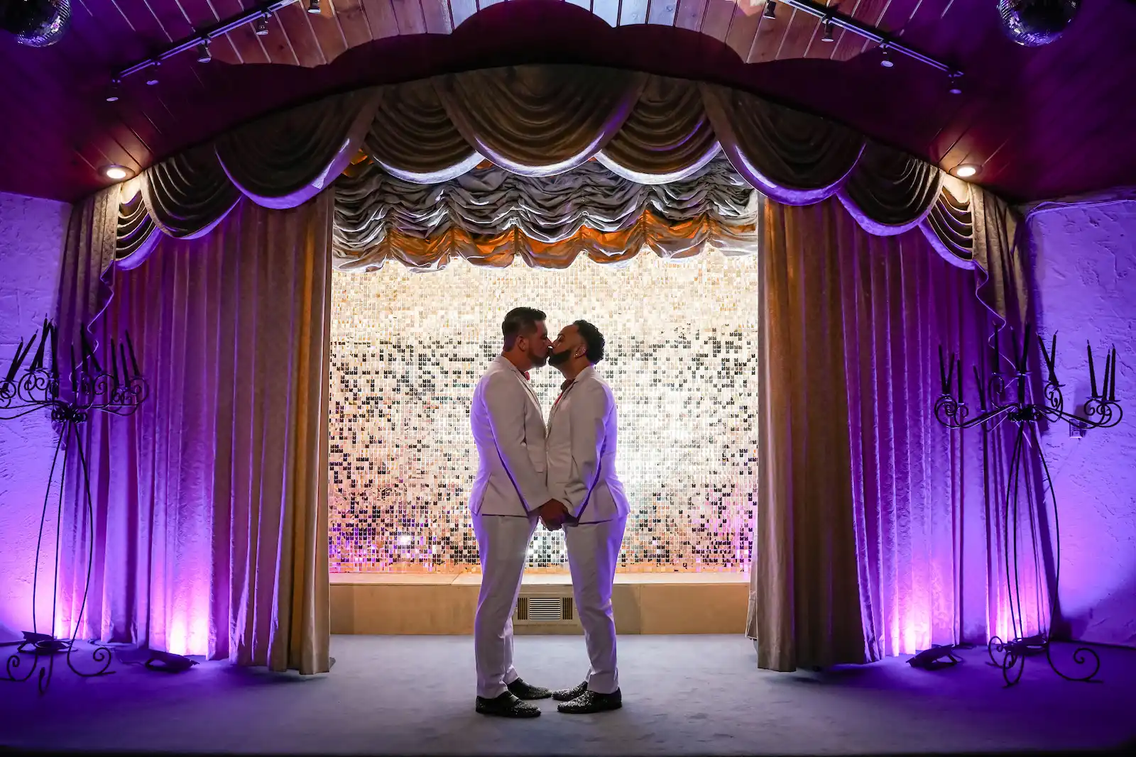 Same-sex couple sharing first kiss on stage at Viva Las Vegas Wedding Chapel with purple uplighting