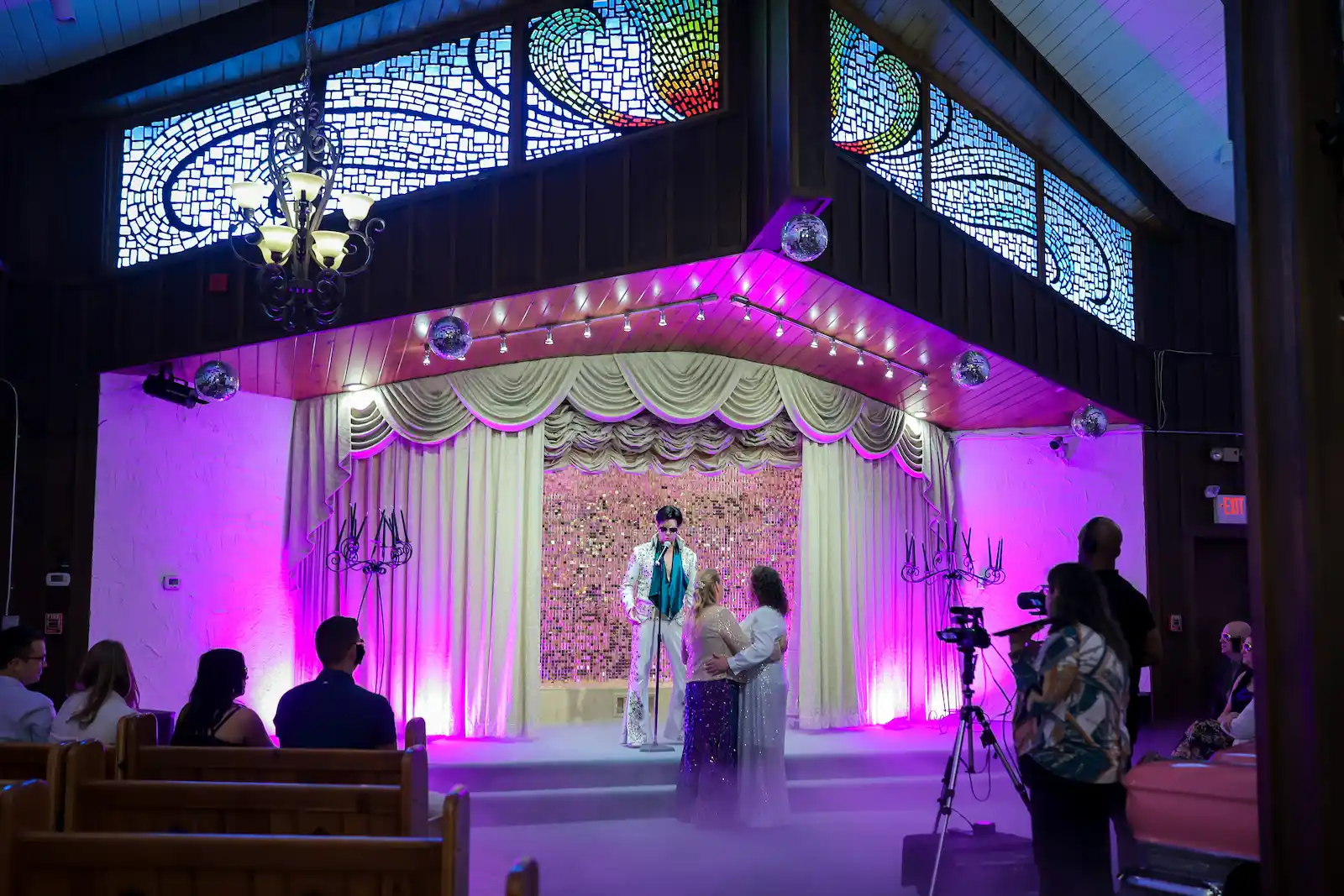 Elvis impersonator officiating wedding ceremony at Viva Las Vegas Wedding Chapel with purple stage lighting and stained glass windows