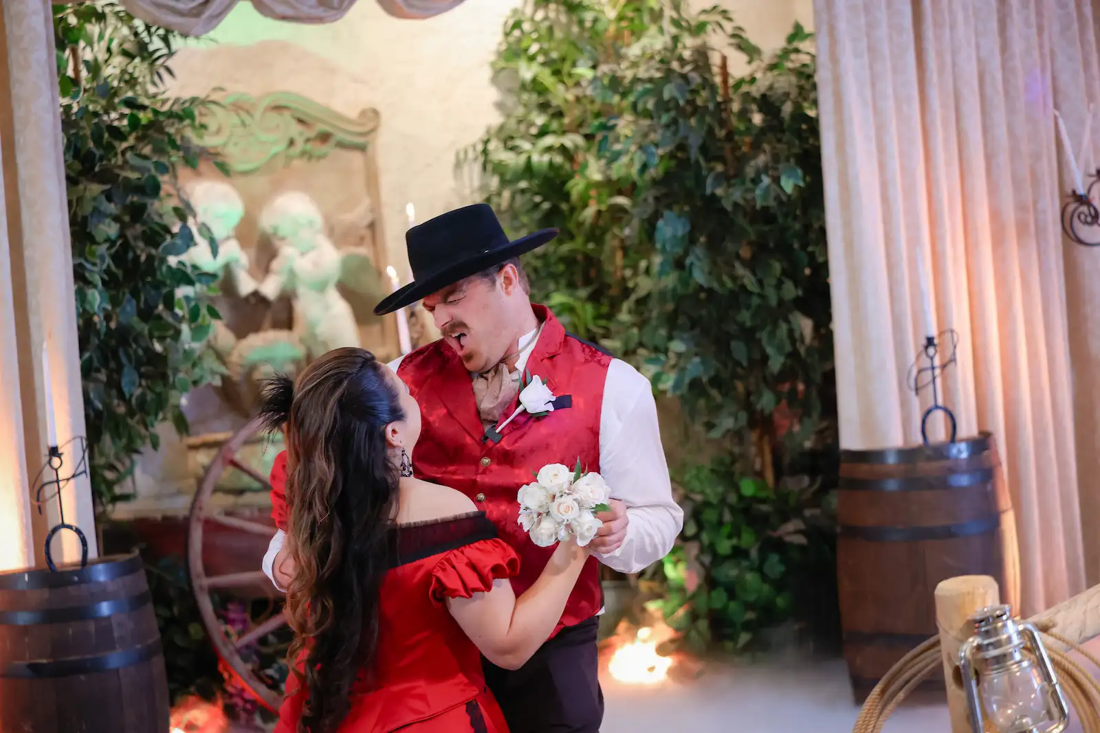 Couple dancing in western outfits with cowboy hat and red dress next to wagon wheel and barrels at a Las Vegas wedding chapel