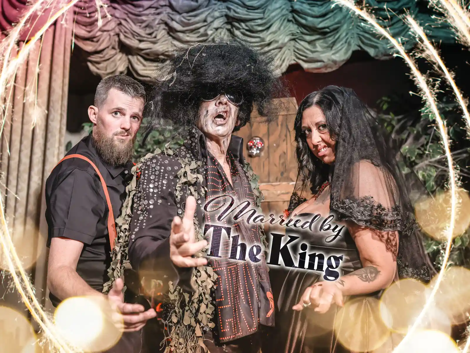 Spooky-themed couple posing with Elvis officiant under sparkler ring reading “Married by The King”