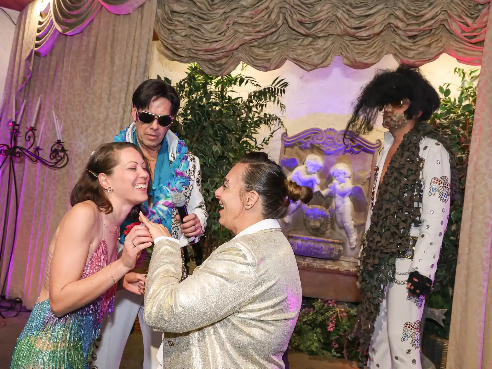 Laughing couple exchanging vows with Elvis officiant and themed performer on chapel stage